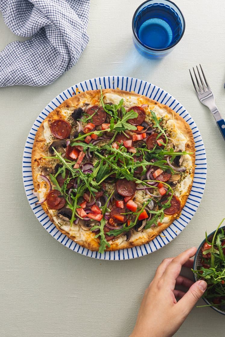 Pizza bianca med pepperoni, sopp og rødløk, toppet med ruccola og tomat