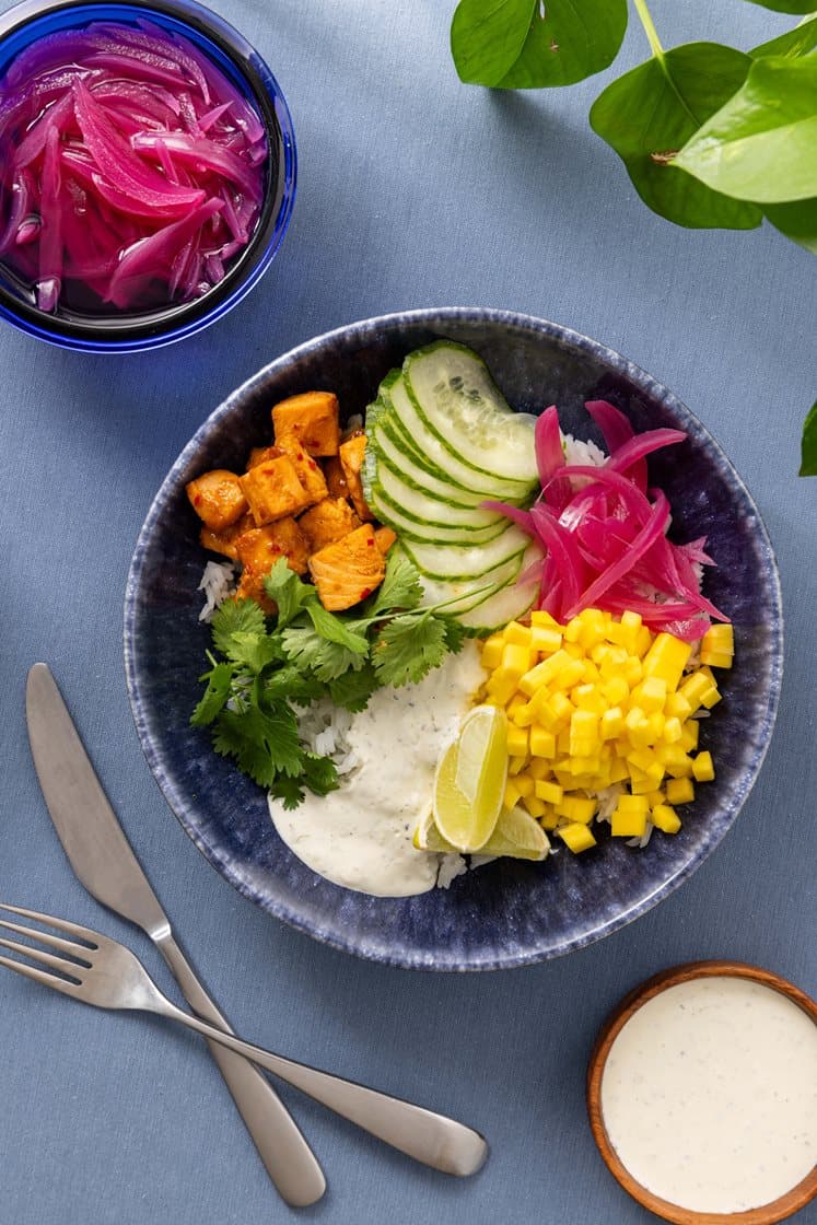 Rice bowl med spicy laks, agurk, mango og syltet rødløk, servert med limerømme og koriander