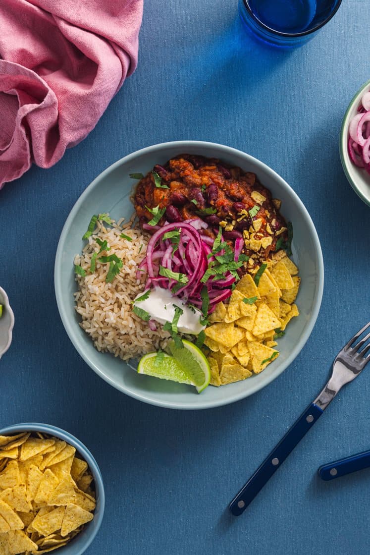 Chili sin carne med fullkornsris, marinert rødløk, tortillachips og rømme, servert med lime